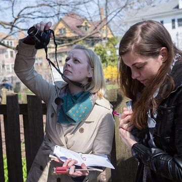 Two students outdoors. One is taking a photo of something out of frame with a camera.