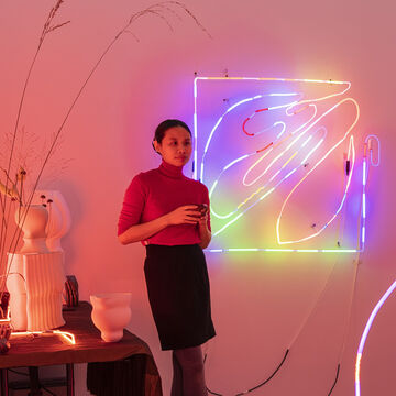Kelly Xi stands next to one of their neon pieces