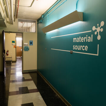 A hallway with a turquoise wall with "Material Source" logo on it