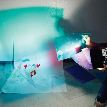 A student using a light with blue tissue paper on the camera lens to create colorful shadow artwork.