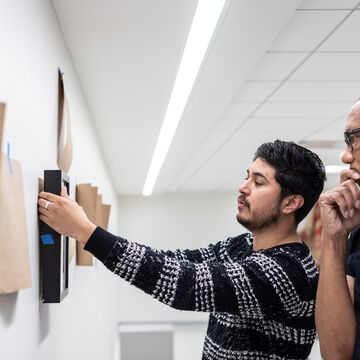 Two people holding up a framed piece of art.