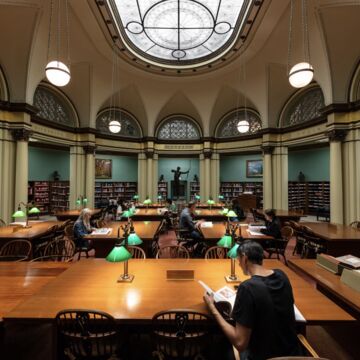 Person reading book sitting at table in large library