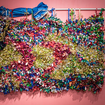 Multi-colored bows covering a large panel hanging on a pink wall using a beach umbrella. 