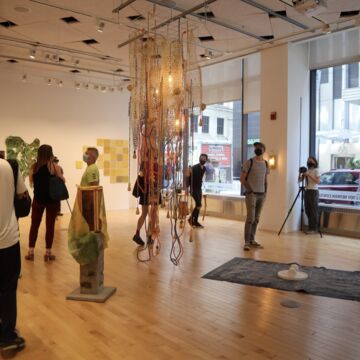 A group of people in a gallery with a large hanging piece of art in the center of the room.