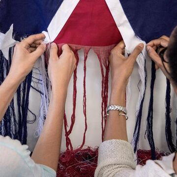 Two people unraveling a Confederate Battle Flag with their hands. 