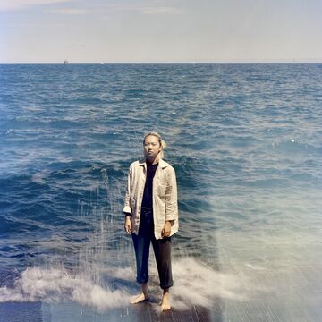 Portrait of a blonde-haired person standing on a concrete platform in front of a lake.