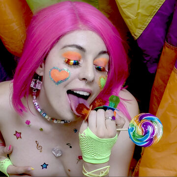 A pink-haired person surrounded by colorful fabric, eating candy