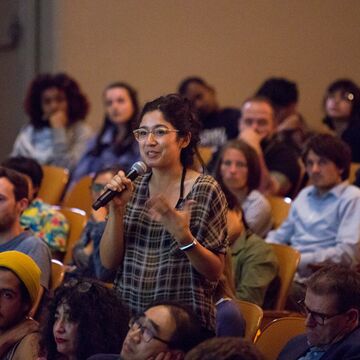 Person standing up in audience talking into a microphone.