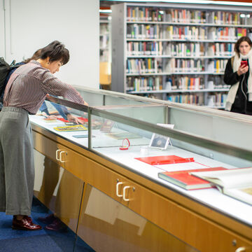Two people looking at books in a glass case inside a library. 