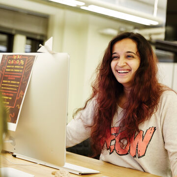 A student sits behind a computer and smiles.