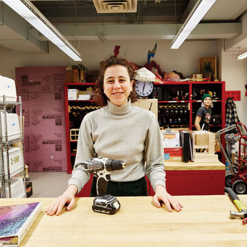 A student working at the media center smiles with a powertool