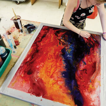 A student painting with bright red and blue on a large canvas.