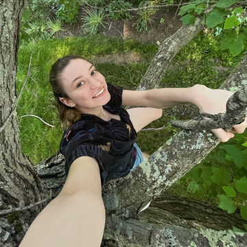 A selfie of a person smiling and sitting in a tree