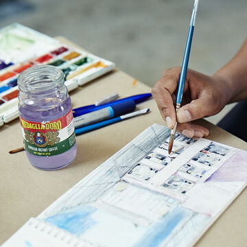 A detailed shot of a person using watercolors to paint a picture in a sketchbook. 