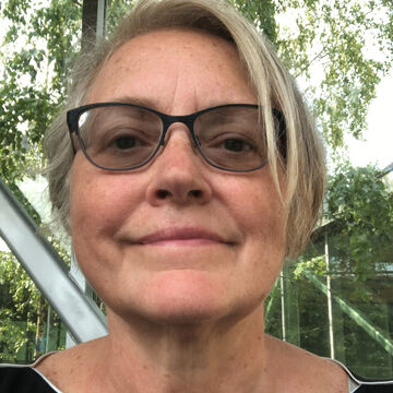 Eia wears dark rimmed glasses and has short blonde hair.
