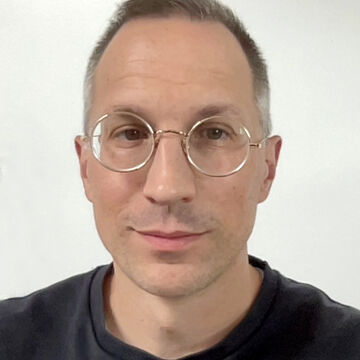 Ryan faces the camera wearing round eye glasses and a black shirt.