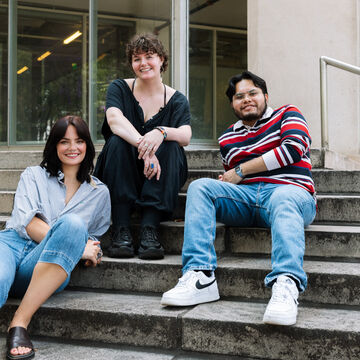 Three SAIC students smile as they sit on the steps of SAIC's campus.