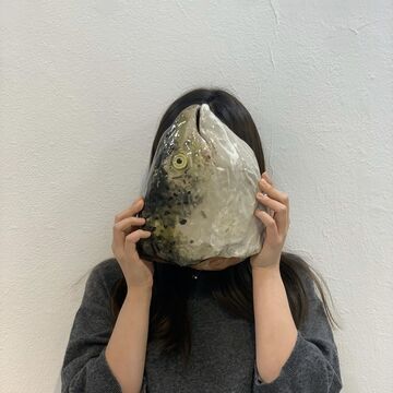 A person holding a ceramic fish head in front of their face