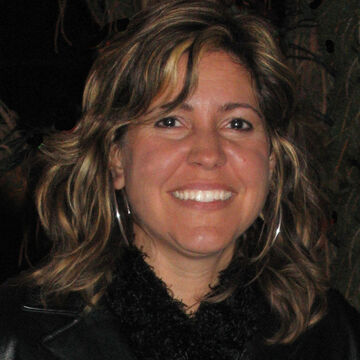 Kimberly Viviano smiles at the camera. She wears a black top and large hoop earrings.