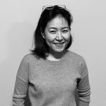 Black and white photo of a smiling Yoonshin Park. She has shoulder length hair and glasses on top of her head.