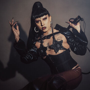 Ale dresses as their drag persona, Celeste, wearing a high dark ponytail and short bangs.