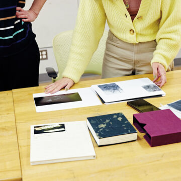 Two people standing at a table looking at documents and books