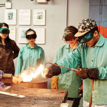 Four students wearing safety equipment and welding metal 