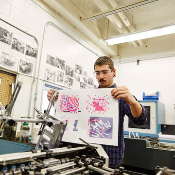 A white man holding a print inside a printmaking facility