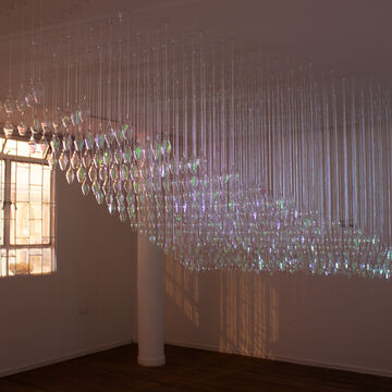 Installation of suspended rows of glass vessels with translucent paper inside of them creating a glimmering appearance.