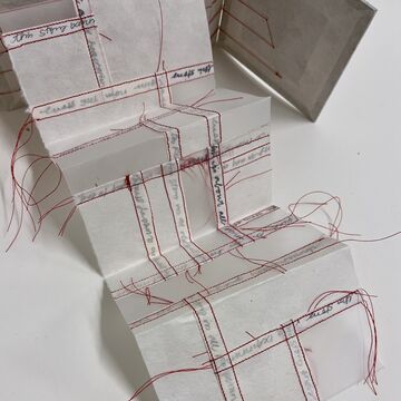 Embroidered fiber art book with red and black text.