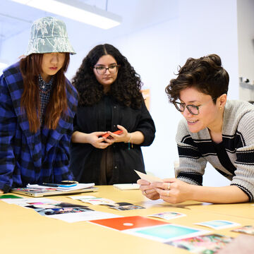 A Visual Communications Design instructor and three students stand around a table looking at images.