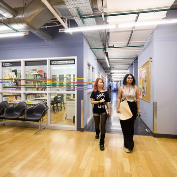 Two students walk down a hallway next to a classroom with glass windows.