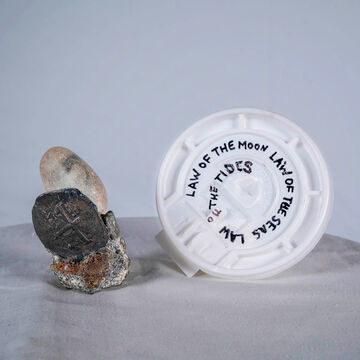A rock and a plastic coffee cup lid on a table.