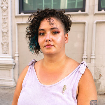 Portrait of Angela Fegan, an adult person with a light-medium skin tone and short dark curly hair.