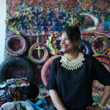 Portrait of Dr. Kymberly Pinder, an adult Black woman with a black updo, smiling in front of a large textile artwork.