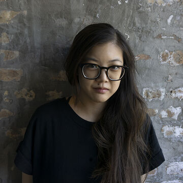 Headshot of L Koo, a fair-skinned brunette Asian adult wearing glasses.