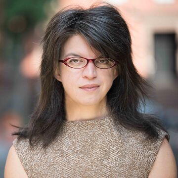 Outdoor headshot of Lindsay Kelley, a fair-skinned adult person wearing glasses with medium-length black and gray hair.