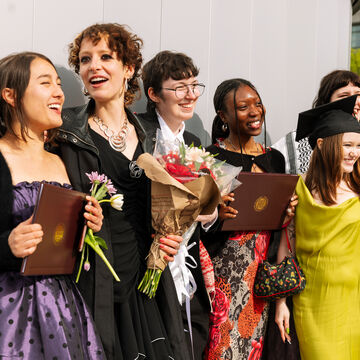 A group of six recent graduates, varying in ethnicity and gender, posing for photos while holding degrees and flowers. 