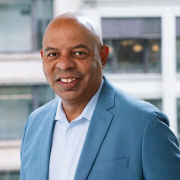 Portrait of Rob Flot, an adult medium-dark skinned person with a bald head smiling.