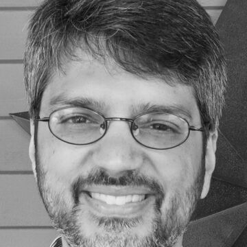 Black and white portrait of Saul Thomas, an adult person with a medium-fair skin tone, glasses and short dark hair.