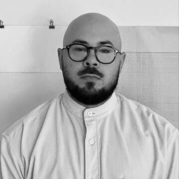 Black and white portrait of Cody Tyler Schueller, an adult person with a medium-fair skin tone, glasses, a bald head, beard and mustache. 