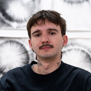 Headshot of an adult person with a fair skin top, cropped brown hair, and a mustache.
