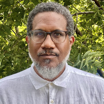 SAIC faculty member Andres Hernandez with medium-dark skin tone, dark hair, a beard, and glasses standing outside.