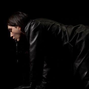 Camila on all fours dressed in black leather, clicking her mouth like a horse. 
