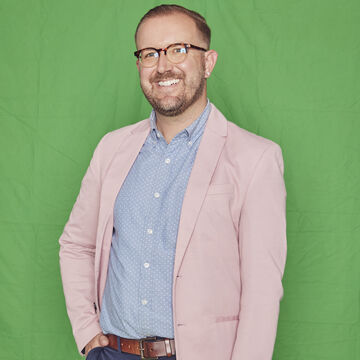 SAIC faculty member Adam Greteman, a person with light skin tone, light hair, and glasses, standing against a green backdrop.