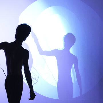 Hesam performing with a microphone. Lights and shadows bounce across the wall. 