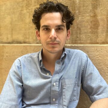 Jake Nussbaum, an adult person with a fair skin tone and short dark wavy hair.