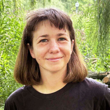 Headshot of Kierstin Siegl, an adult person with a fair skin tone, brown bob, and bangs, smiling in front of a background of greenery.
