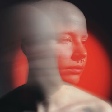 A photograph of Ruby, a bald non-binary person moving their head with long exposure. There is light-leaked effect to the photograph.  