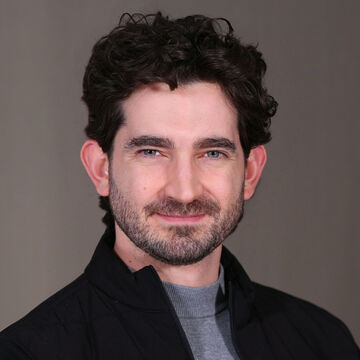 Sebastian Thomas, an adult person with a fair skin tone and dark wavy hair.
